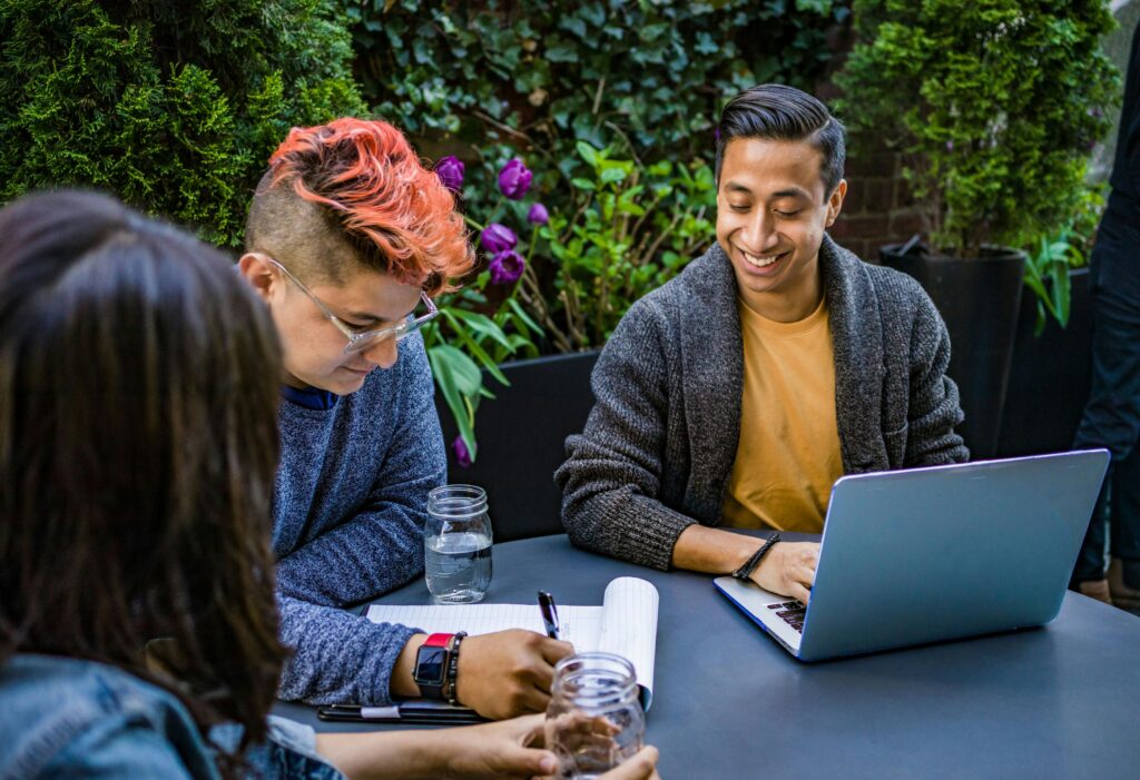 Young professionals working together on a project outdoors with laptops and notebooks in a vibrant garden setting.